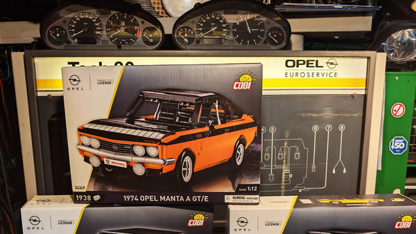 Ein orangenes Klemmbausteinmodell eines Opel Manta A GTE vor einem historischen Opel Tech80 Motortester von SUN